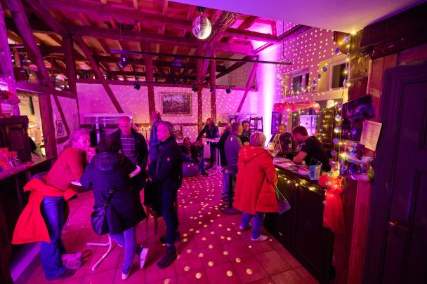 Menschen stehen im bunten Licht an der Bar und unterhalten sich