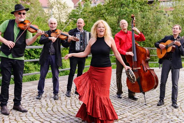 Fünf Musiker und eine Sängerin stehen in einem Halbkreis und musizieren