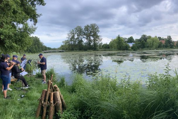 Ein Musikensemble steht am Ufer des Burgsees und Musiziert