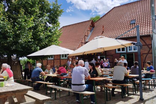Menschen sitzen an Bierbänken unter Sonnenschirmen und unterhalten sich.