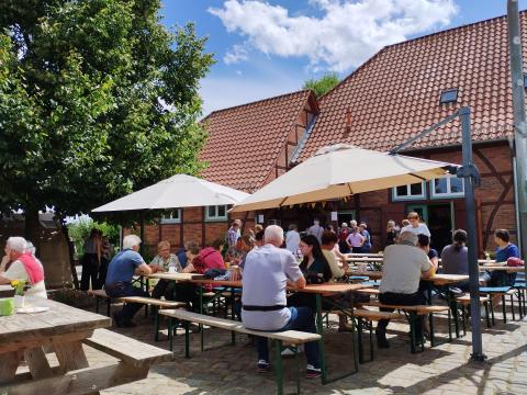 Menschen sitzen an Bierbänken unter Sonnenschirmen und unterhalten sich.